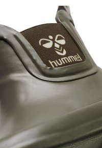 Groene rubberen schoen met een textuur, voorzien van een bruine stoffen label met een reliëflogo. Glad afgewerkt met zachte hoeken en een ronde vorm.