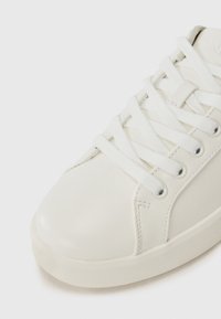 Baskets en cuir blanc avec bout rond, surface texturée et lacets blancs contrastants. Comprend une petite étiquette sur le côté près des lacets.