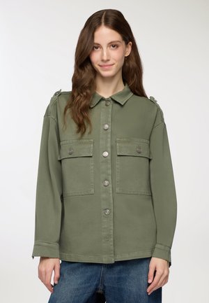 Giacca verde khaki con bottoni frontali, due tasche frontali, spalline e vestibilità rilassata. Tessuto liscio, tessuto resistente e bottoni nascosti.