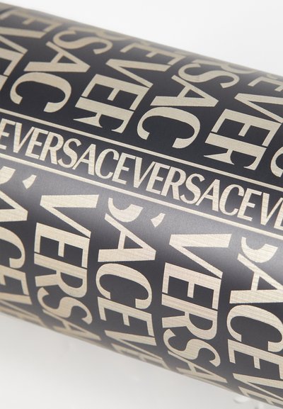Black cylindrical object featuring bold, gold "VERSACE" text in various arrangements against a smooth, matte background.