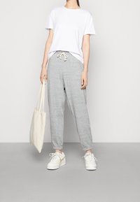 Vit kortärmad t-shirt i kombination med ljusgrå sweatpants med elastiska muddsekla och dragsko, kompletterad med vita sneakers och en tygväska.