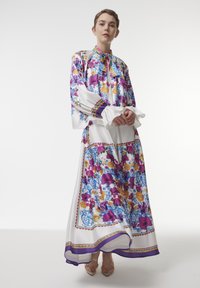 White floral-print dress with purple, yellow, and blue accents, featuring a high collar, puff sleeves, and flowing skirt. Sandals visible.