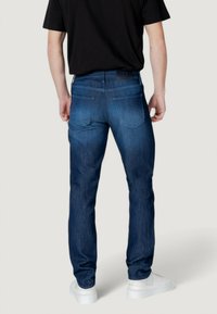 Vaqueros de mezclilla azul oscuro con corte recto, cinco bolsillos y un ligero desgastado. Cuenta con una etiqueta de cuero con la marca en la parte trasera de la cintura.