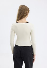 Maglietta a maniche lunghe rigata color beige chiaro con scollatura bassa e rifiniture nere, abbinata a pantaloni neri a vita alta con due tasche posteriori.