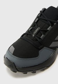 Schwarzer Sportschuh mit strukturiertem Obermaterial, grauen Akzenten und einer stabilen Gummisohle mit sichtbaren Profilmustern. "TERREX"-Markierung sichtbar.