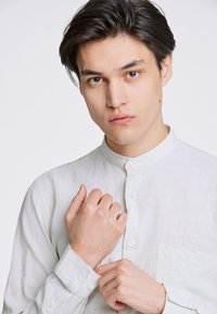 Lichtgekleurde linnen shirt met een bandkraag, doorlopende knoopsluiting en een zakdetail. Glad textuur, casual pasvorm en lange mouwen.