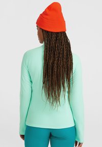 Mintgröna långärmade toppar med en slät textur. Matchas med teal byxor, bärs med en orange mössa. Har en rundad halsdesign.