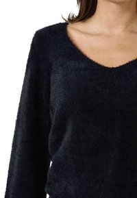Schwarzer, flauschiger Pullover mit V-Ausschnitt und langen Ärmeln. Weiche Textur, lässige Passform und dezenter Glanz. Keine sichtbaren Muster oder Beschläge.