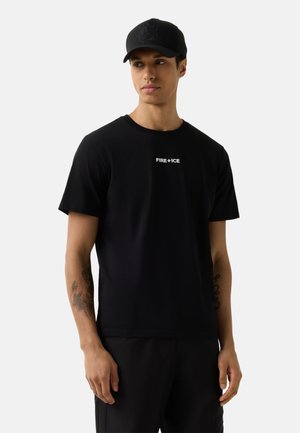 Young man with tattoos wears black cap and black t-shirt with "FIRE+ICE" text, standing against light gray background.