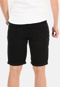 Black denim shorts with rolled cuffs, featuring two back pockets and subtle stitching details. Smooth texture and classic cut.