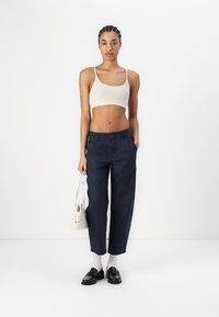 Marineblauwe wijde broek met een hoge taille, gecombineerd met een beige geribde cropped top. De outfit is accessorized met een kleine witte handtas en zwarte instappers.