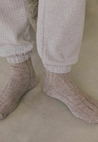 Strukturierte Stricksocken in Hellbraun mit einem gerippten Design, die eng anliegen, kombiniert mit grauen, lockeren Hosen mit einer weichen Textur.