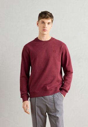 Bordeaux sweatshirt met lange mouwen en geribbelde manchetten. Voorzien van een vierkant logo op de borst en een ronde hals. Gecombineerd met gestreepte broek.