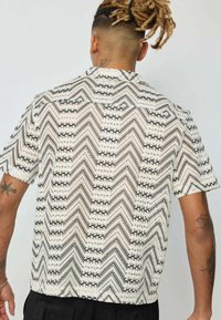 Chemise à manches courtes présentant un motif zigzag noir et blanc avec un tissu texturé ; coutures visibles et col standard.