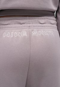 Γκρι παντελόνι jogger Nike Shox με απαλή υφή. Διαθέτει ελαστική μέση και λευκό κεντημένο λογότυπο «NIKE SHOX» στο πί σω μέρος.