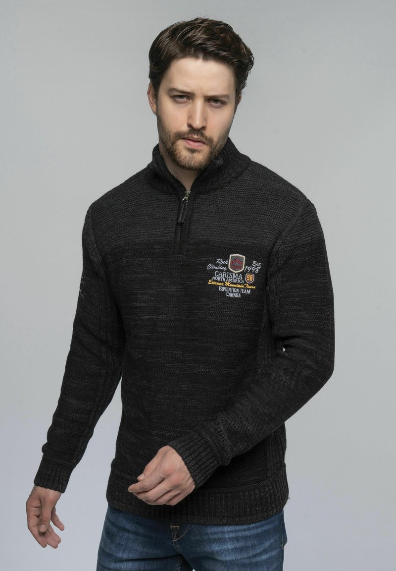 Schwarzer Strickpullover mit einem Viertelreißverschluss-Kragen. Mit gesticktem Text und einem strukturierten Muster. Rippbündchen und -saum.