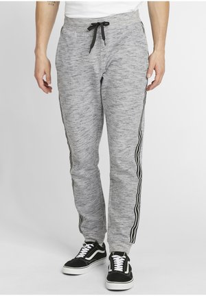 Pantalones de chándal grises con un acabado texturizado, que cuentan con franjas laterales negras, una cintura elástica con cordón y piernas ajustadas. Combinados con zapatillas negras.