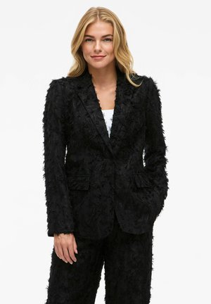 Blazer noir texturé avec un design à franges, doté d'un col cranté et de deux poches avant. Porté avec un pantalon texturé assorti.