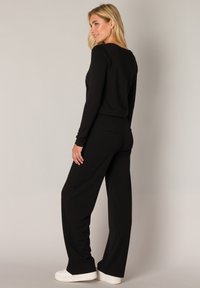 Black long-sleeve top with a round neckline, paired with loose-fitting black trousers. The outfit features smooth fabric and a relaxed silhouette.