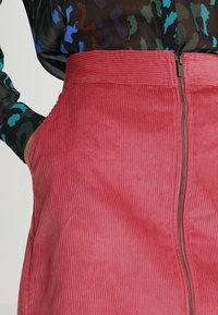 Roze corduroy rok met verticale ribbels, met een verborgen rits aan de achterkant. Bekleed met een aansluitende tailleband voor structuur.