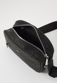 Borsa a tracolla sintetica nera con superficie testurizzata, zip in argento e tracolla regolabile. Interno spazioso con rivestimento in tessuto.