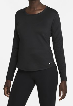 Osoba nosząca dopasowaną czarną koszulkę z długim rękawem oraz czarne legginsy z małym białym logo Nike na dolnej stronie koszulki.
