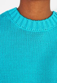 Turkusowy sweter dzianinowy z prążkowanym dekoltem i textured wzorem, prezentujący zbliżenie na kunszt materiału.