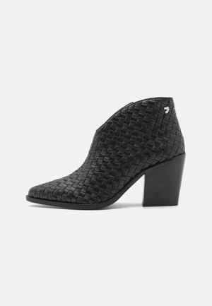 Bottine en cuir tressé noir avec un bout pointu et un talon empilé. Présente un subtil accent métallique près du talon. Texture lisse.