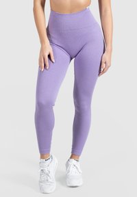 Leggings violettes côtelées avec une taille haute et une texture lisse, associés à des baskets blanches avec des lacets et un logo sur les chaussettes.