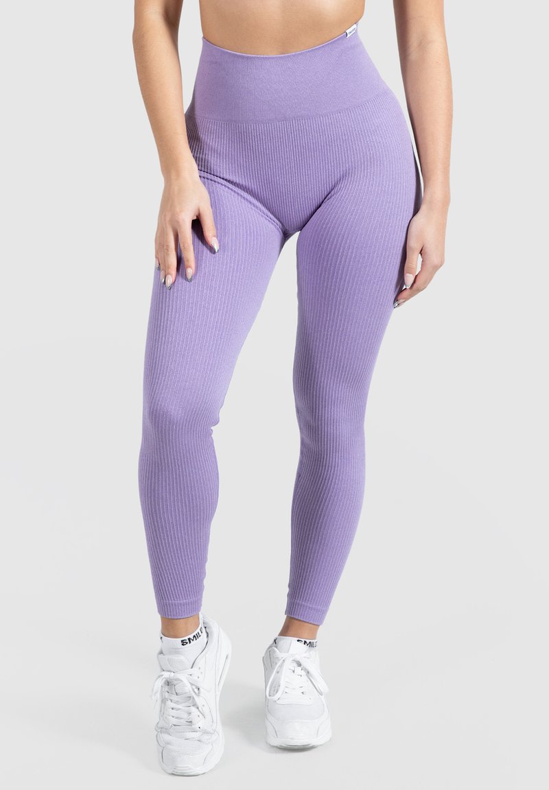 Leggings violettes côtelées avec une taille haute et une texture lisse, associés à des baskets blanches avec des lacets et un logo sur les chaussettes.
