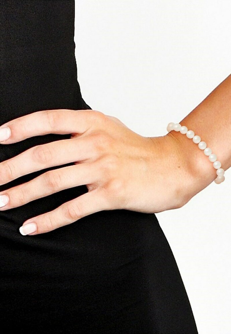 Elastische armband met gladde, glanzende witte kralen, gelijkmatig verdeeld, gedragen aan een hand tegen een zwarte achtergrond.