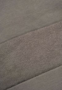 Zbliżenie szarego materiału z trzema wyraźnymi wzorami tkackimi: gładkim, teksturowanym skośnym splotem oraz prążkowanymi krawędziami.