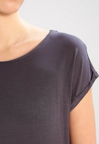 Tmavě šedý top s krátkým rukávem a širokým výstřihem, jemnou texturou a ohrnutými manžetami, který se vyznačuje hladkým a lehkým materiálem.