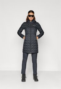 Čierny zateplený dlhý kabát s chevron vzorom, so zipsom a kapucňou. Skombinovaný s tmavými nohavicami a pevnými čiernymi topánkami.