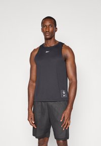 Schwarzes ärmelloses Tanktop mit glatter Textur, mit einem kleinen Markenlogo auf der Brust und einem Etikettendesign am Saum für Details.