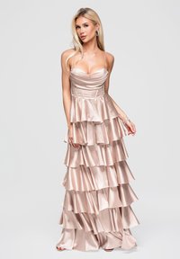 Blonde woman wearing a layered, pale pink satin gown with thin straps and a fitted bodice, standing against a plain light background.