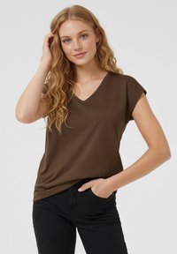 Brun t-shirt med V-ringning och korta ärmar, gjord av mjukt tyg. Bärs med svarta byxor med avslappnad passform och enkel design.