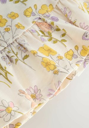 Květinová látka s žlutými a levandulovými květy na krémovém pozadí s nařasenými volány podél okraje, měkká textura.