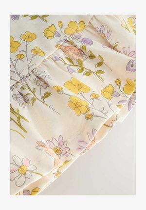 Tissu floral présentant des fleurs jaunes et lavande sur un fond crème avec des volants froncés le long du bord, texture douce.
