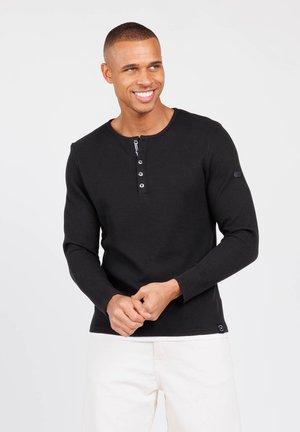 Camisa henley negra de manga larga en tejido texturizado, con cuello redondo, tres botones en la parte delantera y un pequeño logotipo en la manga.