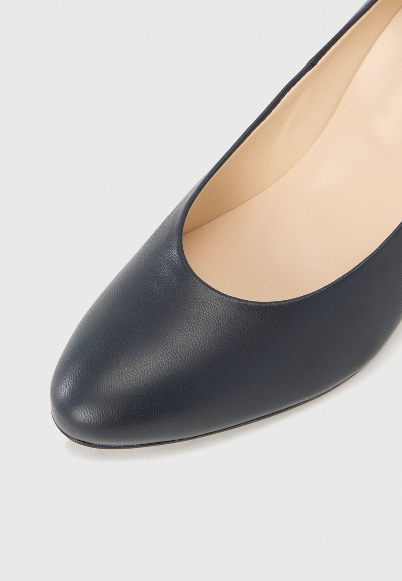 Granatowe skórzane czółenka z okrągłym noskiem i gładką powierzchnią. Wnętrze jest beżowe, prezentując proste, klasyczne wzornictwo.