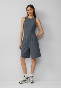 Canottiera grigia con texture a coste abbinata a pantaloni corti coordinati con vita elasticizzata. Il modello indossa sneakers argento e calzini bianchi alla caviglia.