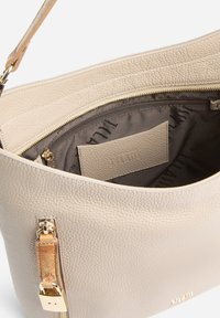 Borsa a mano in pelle beige con finitura testurizzata, chiusura con zip e dettagli in metallo color oro. Interno con fodera in tessuto con logo del marchio e tasca.