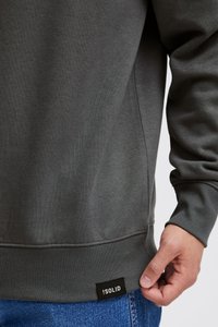 Dark gray sweatshirt made of soft fabric, featuring ribbed cuffs and hem, with a visible black label on the side.
