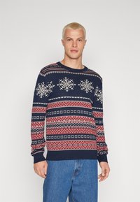 Maglione blu navy con un motivo di fiocchi di neve bianchi, disegni geometrici rossi e bianchi, scollo tondo e maniche lunghe.