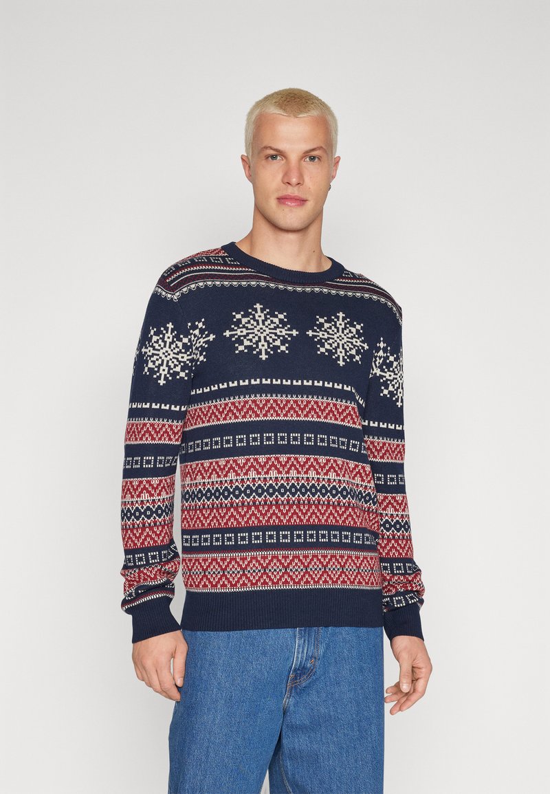 Maglione blu navy con un motivo di fiocchi di neve bianchi, disegni geometrici rossi e bianchi, scollo tondo e maniche lunghe.