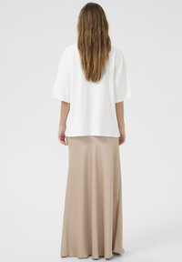 Witte oversized t-shirt met korte mouwen in combinatie met een lange, beige, vloeiende rok, die een zachte textuur en een ontspannen pasvorm toont.