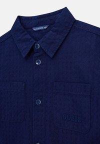 Donkerblauw overhemd met knopen, gemaakt van een structuurstof, met een puntige kraag, twee voorzakken en een geborduurd logo op de linkerzak.