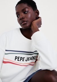 Sudadera blanca con cuello redondo que presenta el texto "PEPE JEANS" y franjas de color verde, rosa y rojo en la parte frontal.