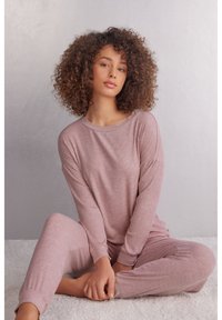 Ljusrosa, ribbad loungeklädsset med långa ärmar och byxor, med en avslappnad passform. Mjuk textur, minimal design och rynkade ärmslut.